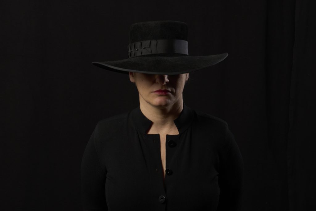 Authentic portrait of a woman in a wide-brimmed hat with red lipstick, showcasing minimalist, expressive photography by Milton Keynes portrait photographer Anna Berry